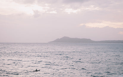 Wide shot of a sea kayaker, crossing in front of an island way in the background.