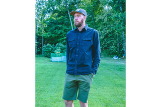 A man in shirt, shorts and cap, standing in a grassed area.