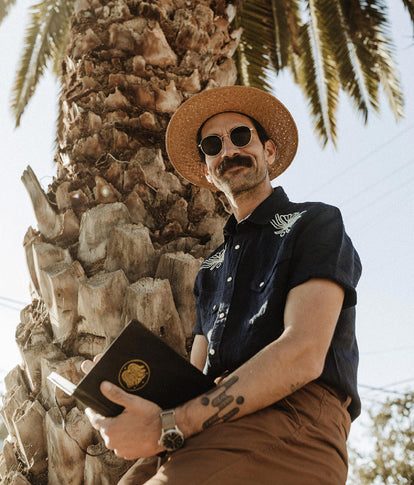 Daren Magee writing in his sketchbook in The Short Sleeve Embroidered Western in Indigo Linen