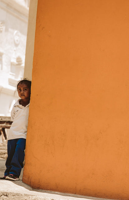 A child leaning on the corner of a bright orange-painted building.