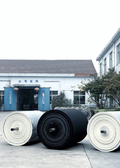 Three large bolts of material outside a factory door.