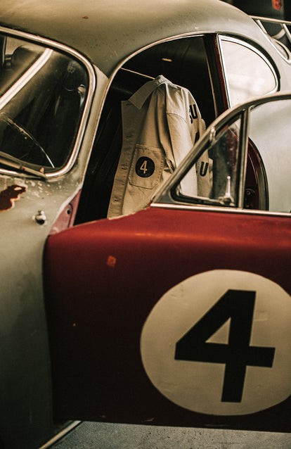 The open door of a vintage Porsche with the Four logo decal upon it and a jacket hanging inside the car with the same logo.