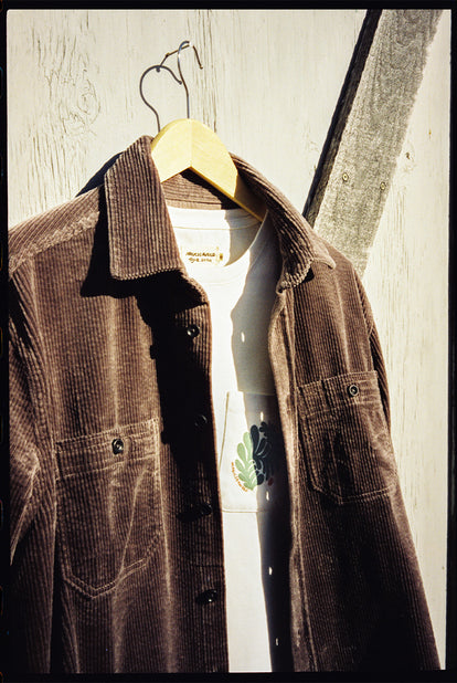 A corduroy shirt over a white tee, hanging against a wooden wall.