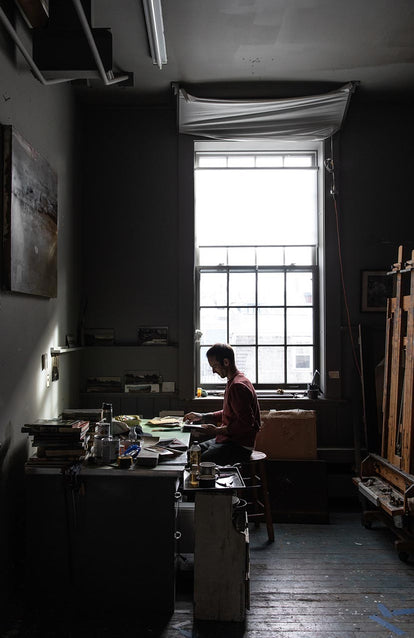 Further away shot of Tim journaling, wearing the crewneck in brick red terry.