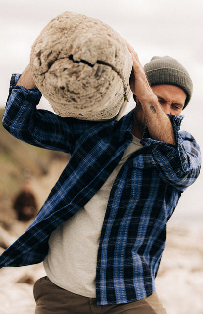 Model carrying a log on his shoulder, wearing The Division Shirt in Rinsed Indigo Plaid