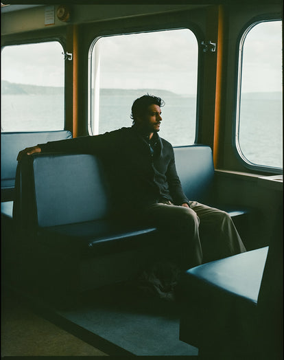 Model sitting in the ferry, wearing The Crawford Sweater in Charcoal