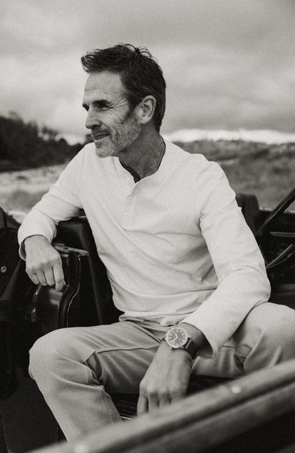 fit model sitting on rocks wearing The Organic Cotton Henley in Vintage White