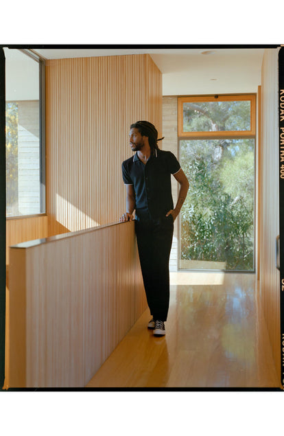 fit model leaning against the wall wearing The Button Down Polo in Coal Herringbone