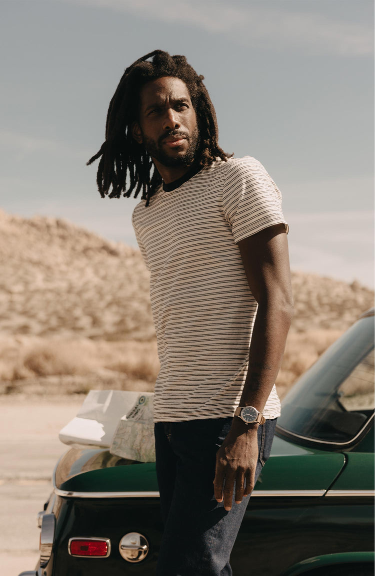 fit model posing next to a car wearing The Cotton Hemp Tee in Black Coffee Stripe