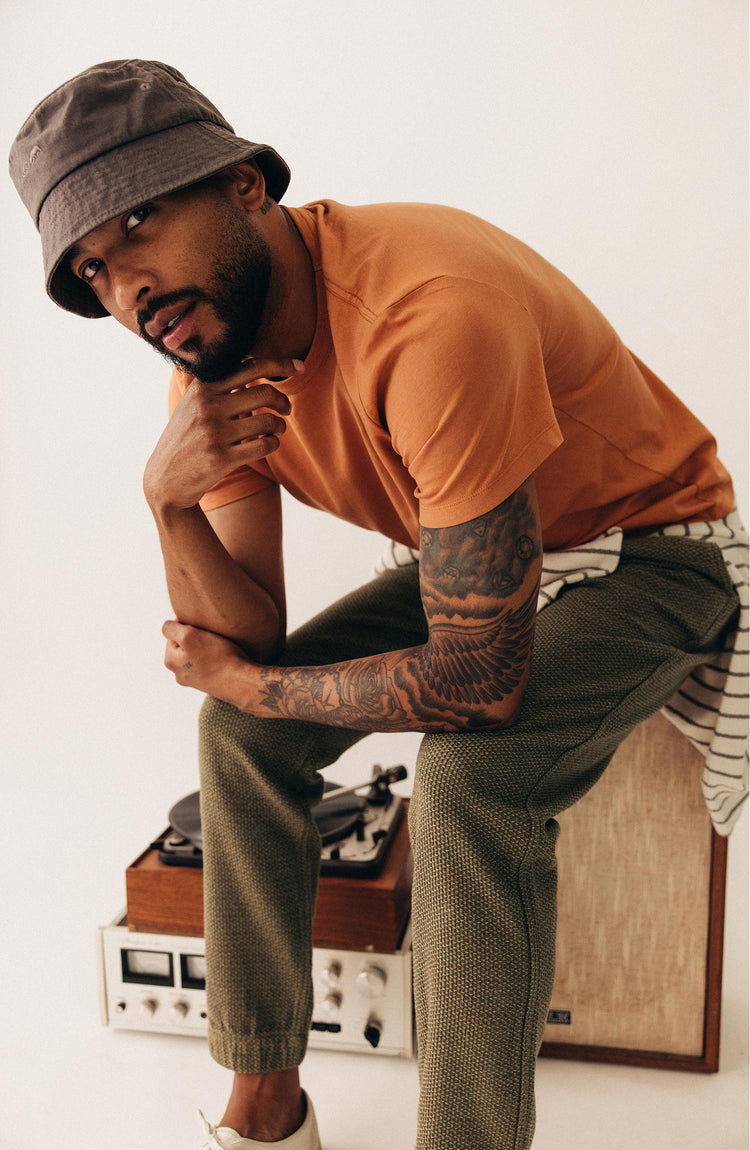 fit model sitting on a speaker wearing The Organic Cotton Tee in Adobe