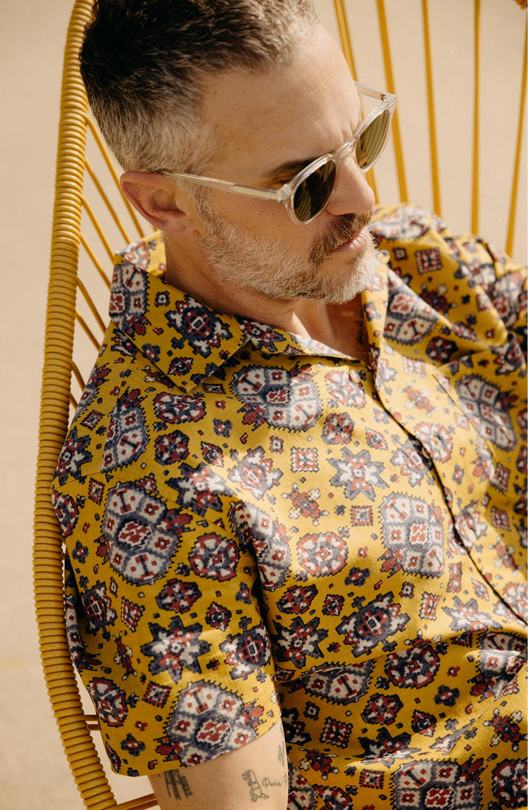 fit model sitting on a chair wearing The Short Sleeve Davis Shirt in Tarnished Gold Print