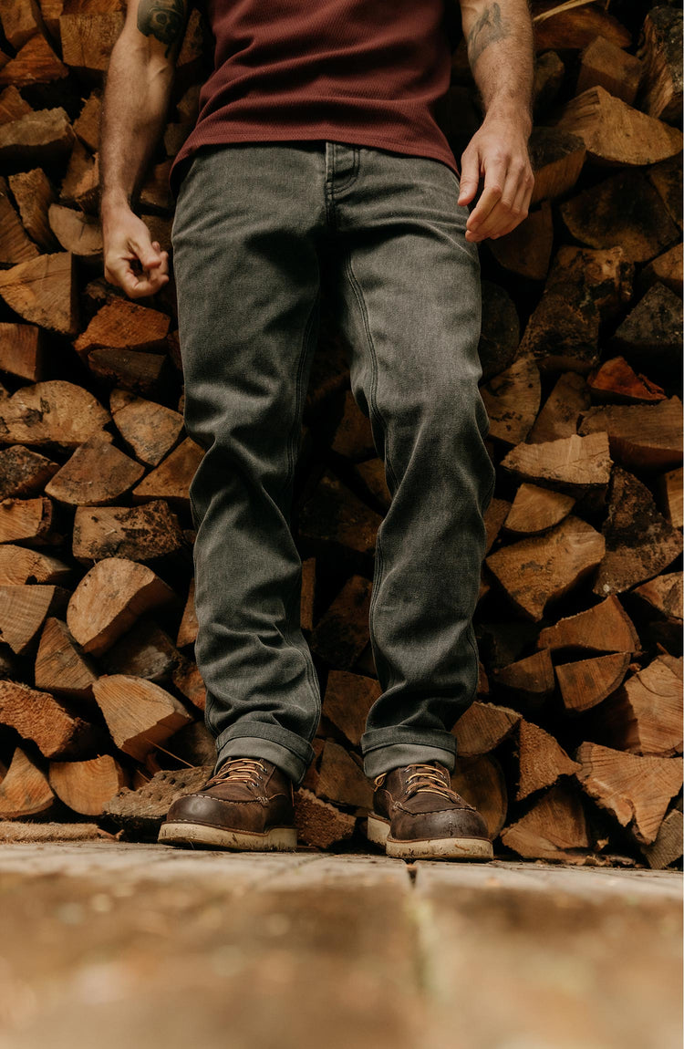 fit model leaning against a wood pile wearing The Camp Pant in Coal Chipped Canvas