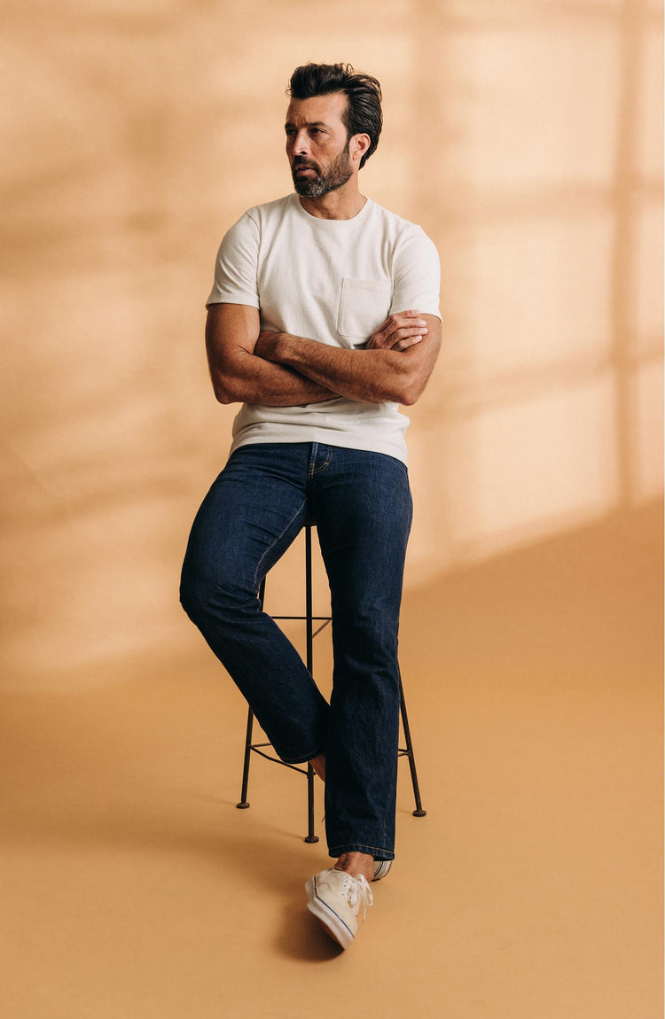 fit model sitting on a stool wearing The Heavy Bag Tee in Natural