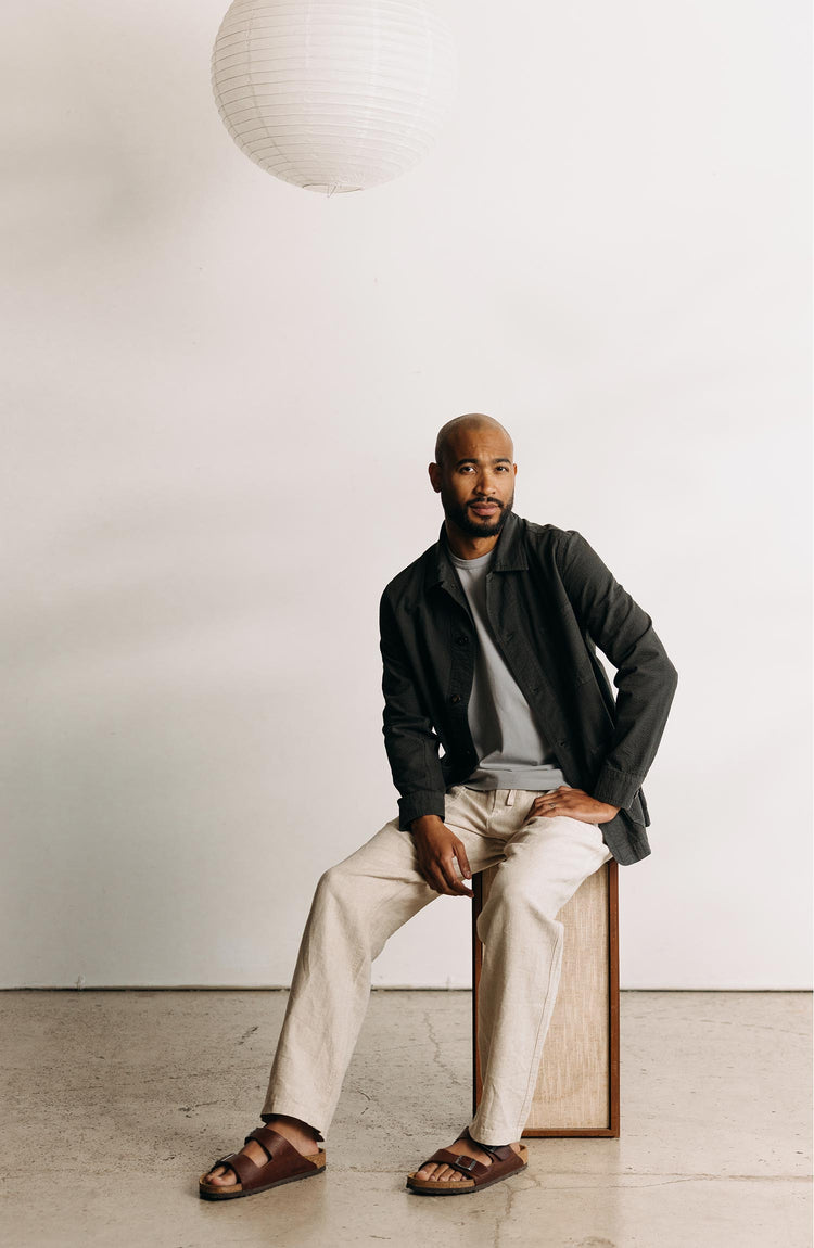 fit model sitting on a speaker wearing The Ojai Jacket in Faded Black Seersucker