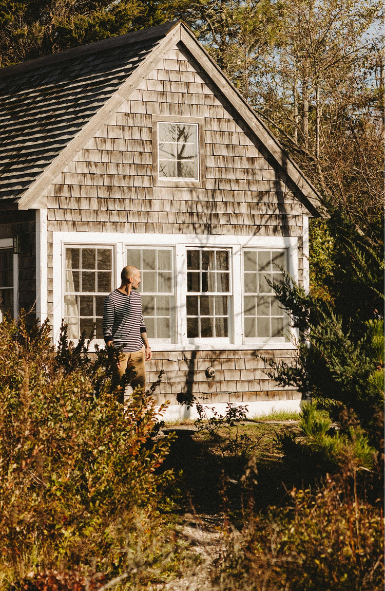 fit model posing in front of a house wearing The Organic Cotton Henley in Rinsed Indigo Stripe