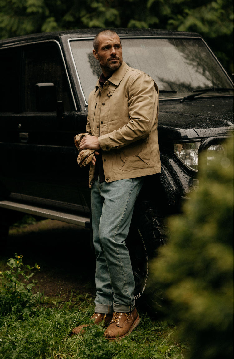 fit model leaning against a car wearing The Pathfinder Jacket in Khaki Dry Wax