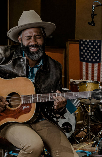 Our man playing an acoustic guitar, feeling it, with musical instruments and Americana in the background.