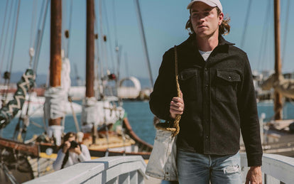 Our guy walking towards the camera toting a rope-handled bag, with a blurred marina scene in the backround.