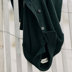 The Harbor Sweater Jacket in Black Pine Heather hanging on a fence, Knits by Taylor Stitch