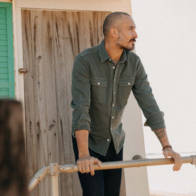 fit model leaning on a pole wearing The Ledge Shirt in Deep Sea Twill, Wovens by Taylor Stitch