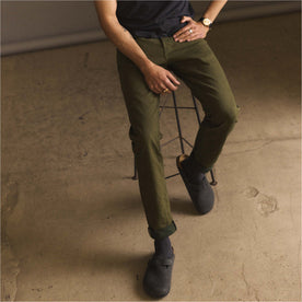 fit model sitting on a stool wearing The Slim Jean in Olive Nihon Menpu Selvage, Bottoms by Taylor Stitch