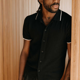 fit model leaning against the wall wearing The Button Down Polo in Coal Herringbone, Knits by Taylor Stitch