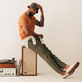 fit model sitting on a speaker wearing The Organic Cotton Tee in Adobe, Knits by Taylor Stitch