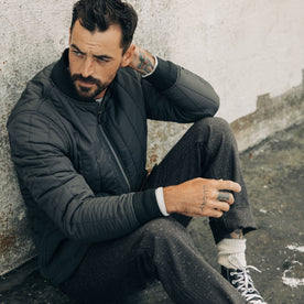 fit model sitting in The Able Jacket in Faded Black Quilted Nylon, Outerwear by Taylor Stitch