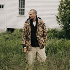 fit model standing in a field in The Explorer Jacket in Vintage Arid Camo Dry Wax, Outerwear by Taylor Stitch