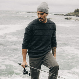 fit model holding a fishing rod in The Lodge Sweater in Charcoal Stripe, Knits by Taylor Stitch