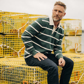 fit model sitting on fishing boxes wearing The Rugby in Dark Forest Stripe, Knits by Taylor Stitch