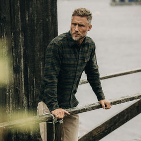 fit model leaning against a wooden railing in The Yosemite Shirt in Dark Forest Plaid, Wovens by Taylor Stitch