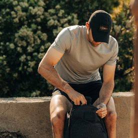 fit model zipping up a backpack wearing The Performance TAC Hat in Black, Accessories by Taylor Stitch