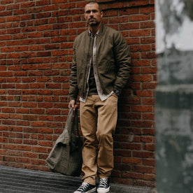 fit model leaning against a wall in The Insulated Bomber Jacket in Fatigue Olive Dry Wax, Outerwear by Taylor Stitch