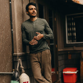 fit model leaning against the wall wearing The Merino Henley in Heather Army, Knits by Taylor Stitch