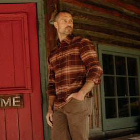 fit model leaning against the wall wearing The Ledge Shirt in Chestnut Plaid, Wovens by Taylor Stitch