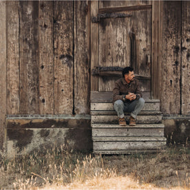 fit model sitting outside a barn in The Longshore Jacket in Aged Penny Chipped Canvas, Outerwear by Taylor Stitch