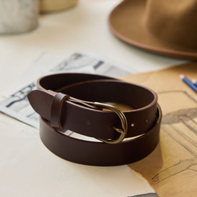 editorial image of The Foundation Belt in Dark Brown rolled up on sheets of paper, Accessories by Taylor Stitch