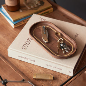 The Valet Tray in Walnut and Brass on a book, Accessories by Taylor Stitch