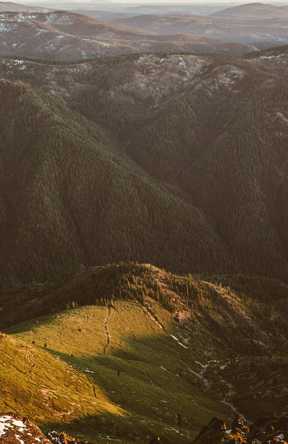 An aerial shot of a mounting forest, with light snow in the distance.