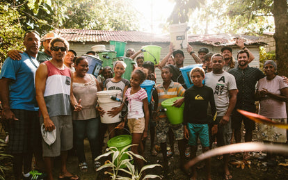 The team, twenty or so strong, carrying buckets and posing outside in a rural jungle setting.