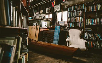 Several bookshelves surrounding two map-drawer chests, topped with assorted marine paraphenalia, against a wall hung with similar-themed photos and curios.