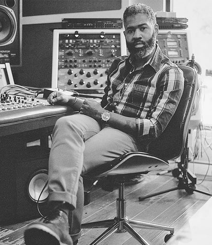 A black and white shot of our man seated at a recording studio mixing desk.