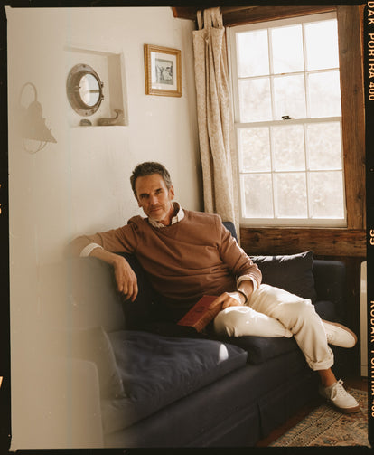 Model sitting on the couch with a book in The Cotton Hemp Crew in Faded Brick