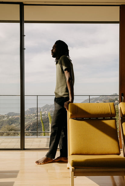 Model leaning against a chair, wearing The Valencia Sweater Polo and The Thomas Trouser