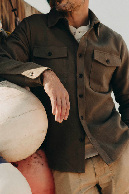 Model leaning against a buoy in The Maritime Shirt Jacket in Fatigue Olive