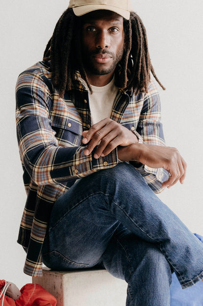 Model sitting in the studio in The Ledge Shirt in River Plaid and Pathfinder Cap in Khaki Dry Wax