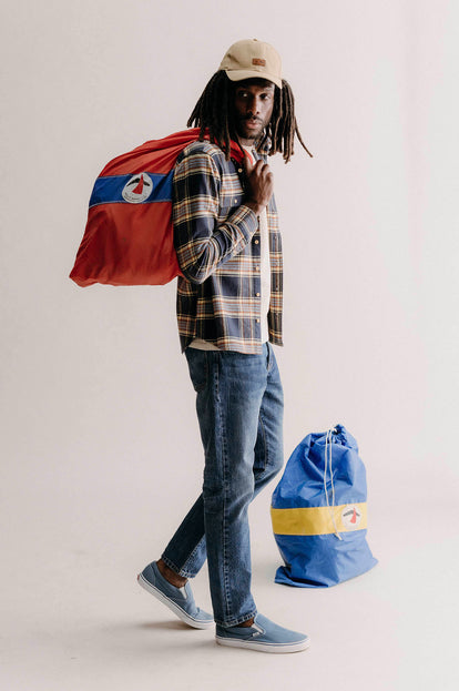 Model carrying a sail bag in The Ledge Shirt in River Plaid and Pathfinder Cap