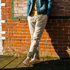 fit model wearing The Democratic Foundation Pant in Organic Stone leaning against a brick wall, Bottoms by Taylor Stitch