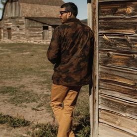 fit model leaning up against barn in The Field Jacket in Camo, Outerwear by Taylor Stitch